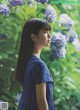 A woman in a blue dress standing in front of a bush of flowers.