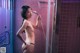 A naked woman standing in a shower holding a shower head.