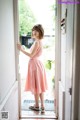 A woman in a pink dress standing in an open door.